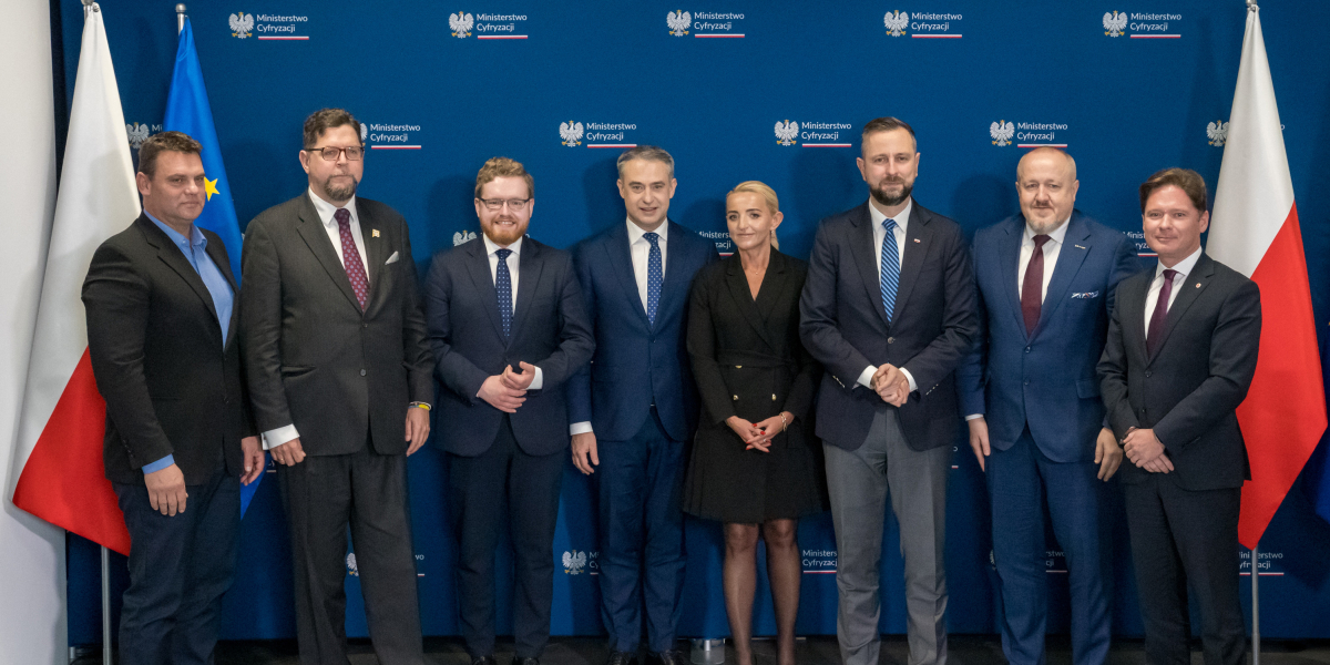 Grupa osób pozująca do zdjęcia przy granatowej ściance