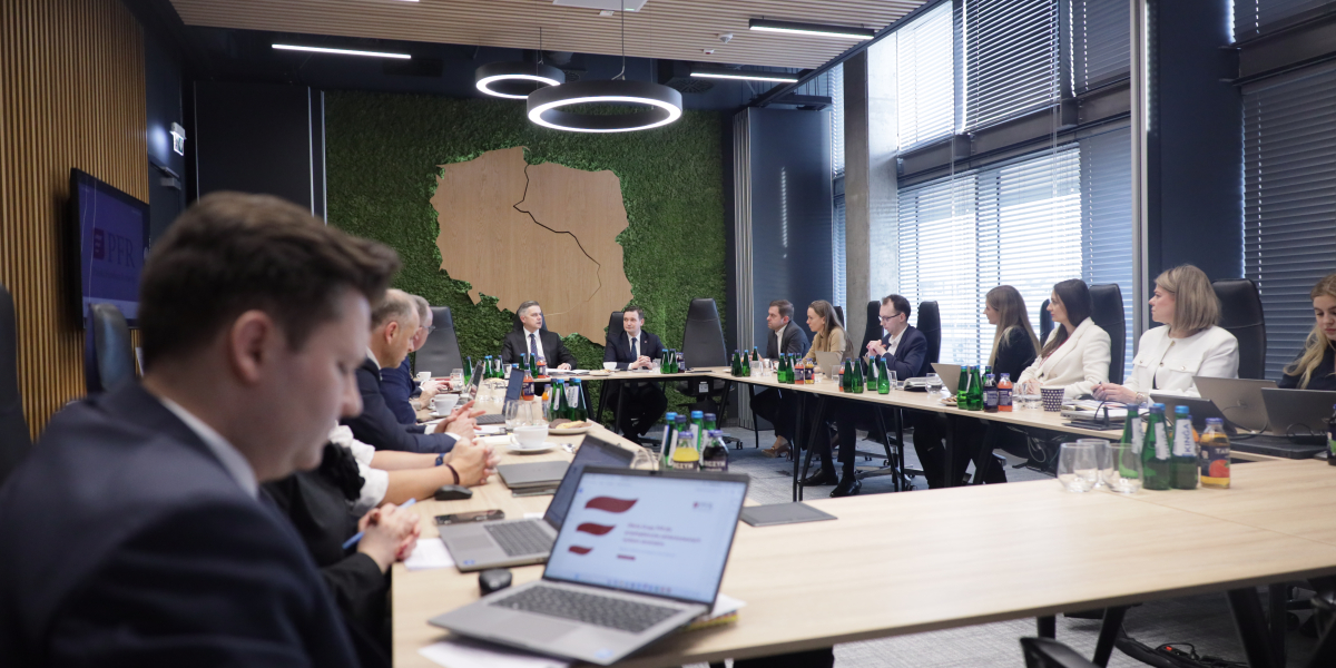 Grupa osób siedzących przy stołach ustawionych w dużej sali