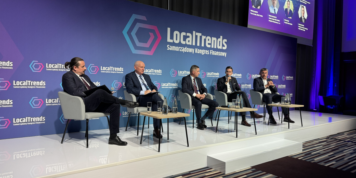Grupa osób siedzących na krzesłach na scenie