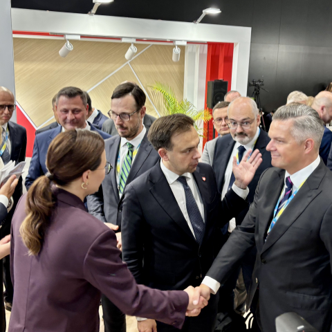Tłum ludzi, a wśród nich mężczyzna i kobieta witający się poprzez uścisk dłoni.